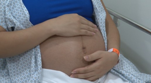 Com roupa de hospital, mulher na reta final da gravidez coloca a mão na barriga