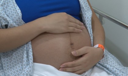 Com roupa de hospital, mulher na reta final da gravidez coloca a mão na barriga