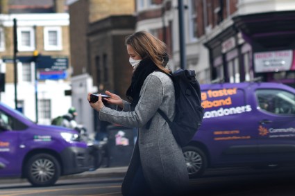 Mulher usa máscara enquanto caminha por Londres de olho no celular