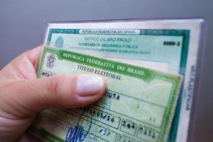 Mão segurando título de eleitor e RG