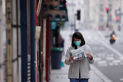 Mulher usando máscara protetora lê o jornal em rua deserta de Paris, França