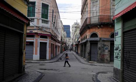 Mulher usando máscara anda ao lado das lojas fechadas no centro do Rio de Janeir
