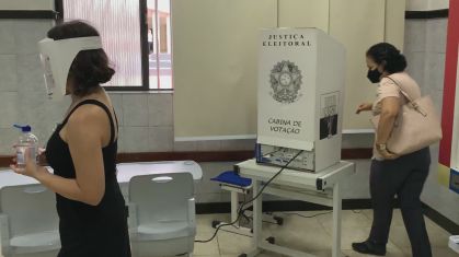 Eleitora e mesária cumprem as protocolos de segurança em local de votação