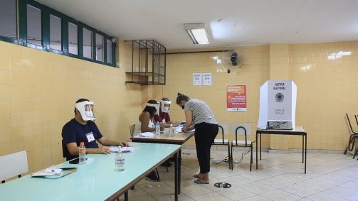 Mesários equipados com face shield em local de votação