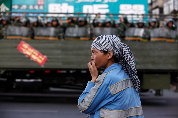 Mulher uigure na beira da estrada enquanto polícia paramilitar chinesa passa dentro de caminhão em rua de Urumqi, na região de Xinjiang, na China / Foto: Nir Elias/Reuters (9.jul.2009)