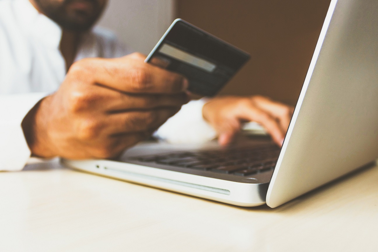 Pessoa segura cartão em frente a computador. E-commerce, venda online