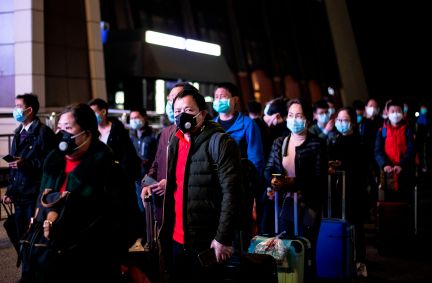 Passageiros usam máscaras faciais enquanto formam uma fila em Wuhan