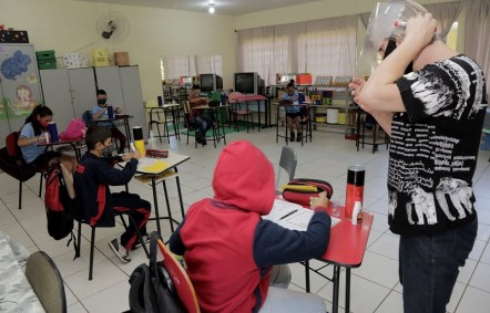 Professora orienta aluno em aula preparada com proteção e distanciamento