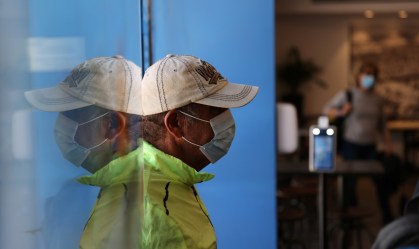 Homem usando máscara é refletido no vidro ao entrar em espabelecimento de Israel