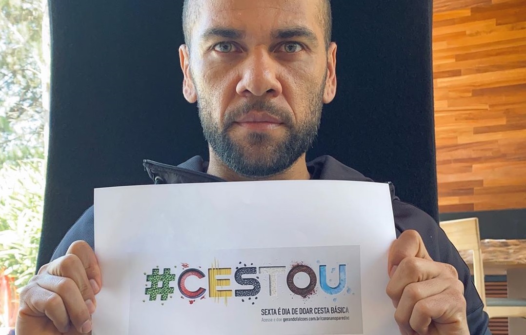 Daniel Alves mostra cartaz da campanha #cestou, que doa cestas básicas