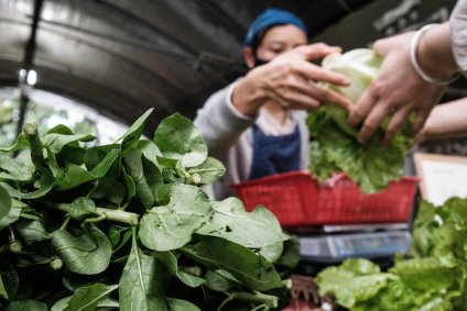 Mulher vestindo máscara vende legumes em uma fazenda comunitária em Hong Kong