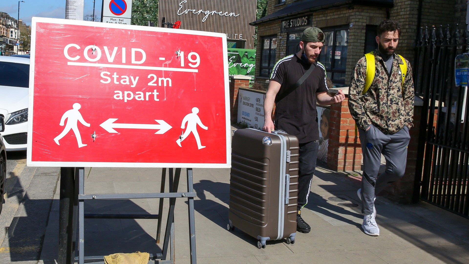 Homens caminham por Londres ao lado de placa que pede distanciamento social