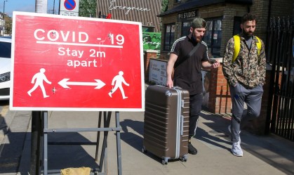 Homens caminham por Londres ao lado de placa que pede distanciamento social