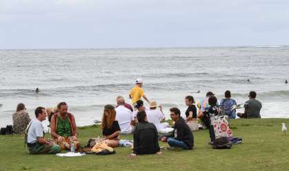 Pessoas sentam na grama ao lado da praia em Byron Bay, na Austrália