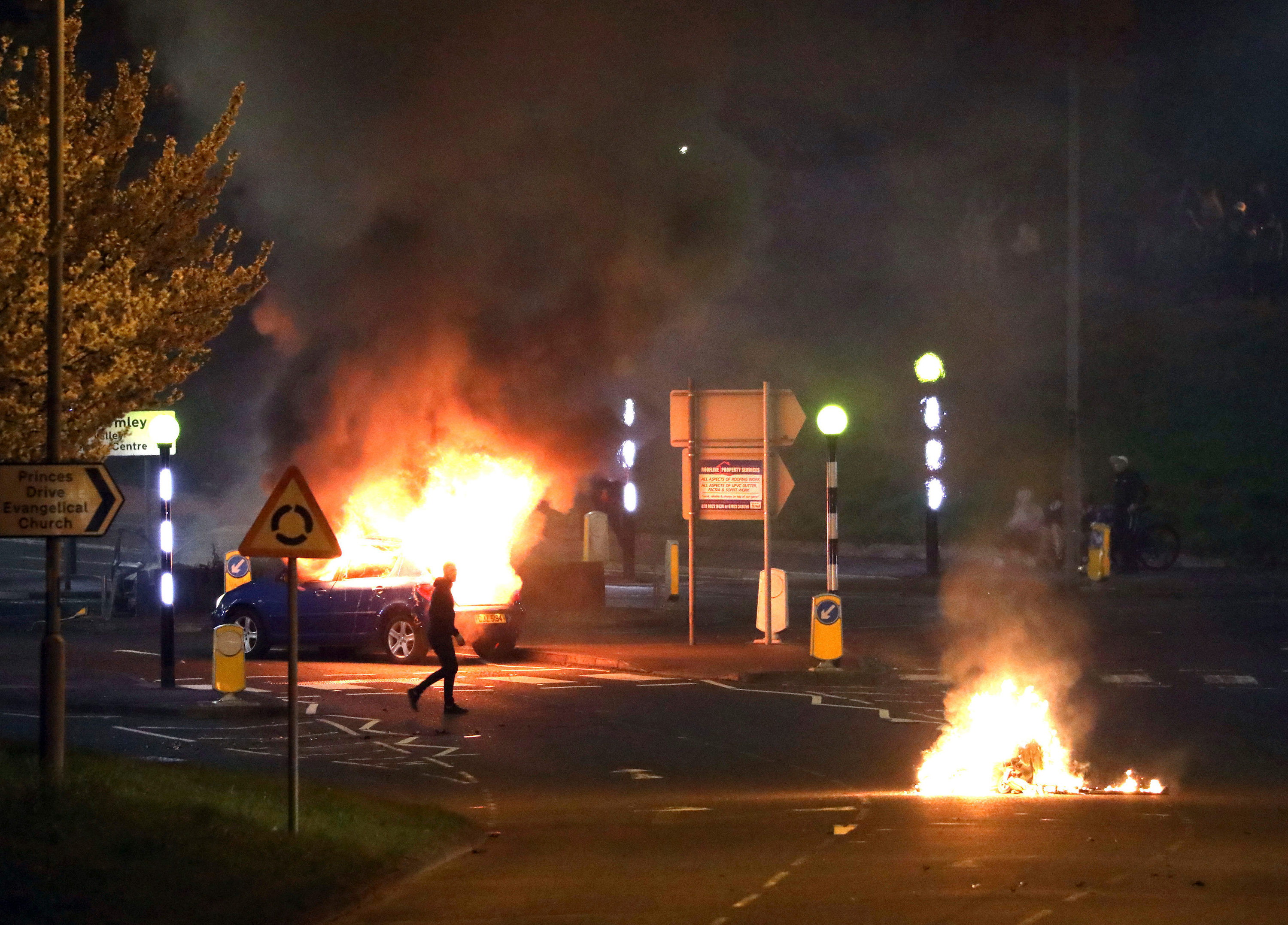 Homem caminha na frente de carro pegando fogo em Belfast, no norte da Irlanda / Foto: Peter Morrison/AP (3.abr.2021)