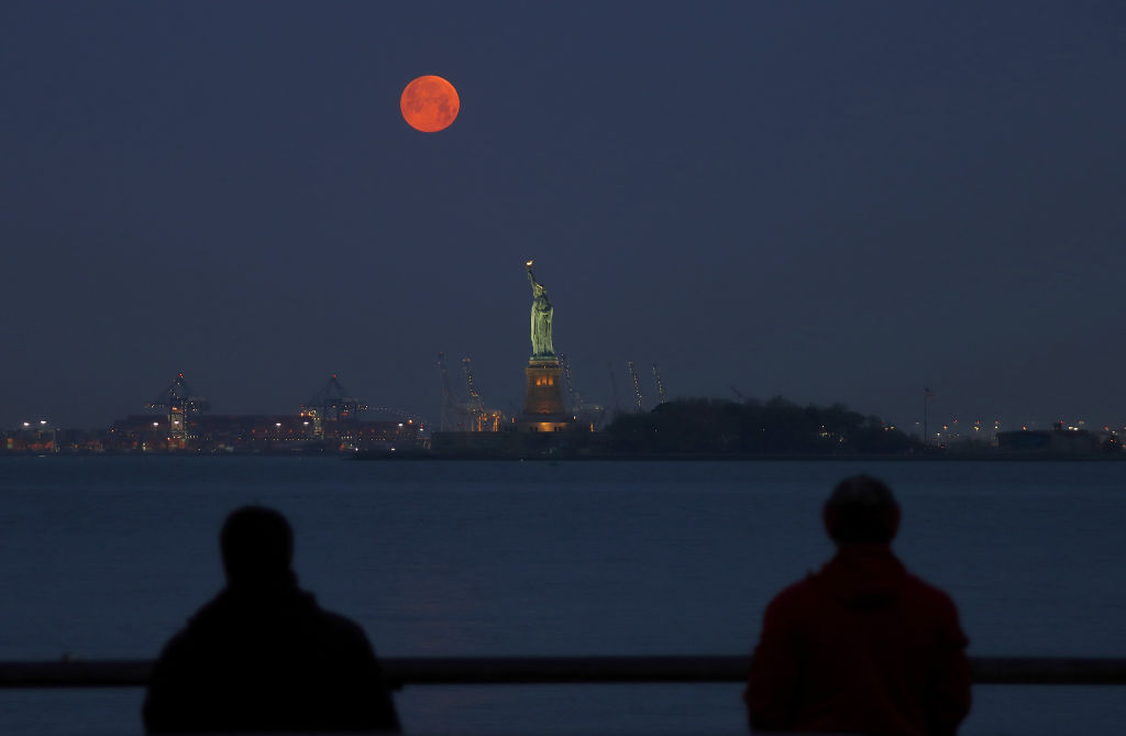 Dois pescadores observam a superlua atrás da Estátua da Liberdade, em Nova York