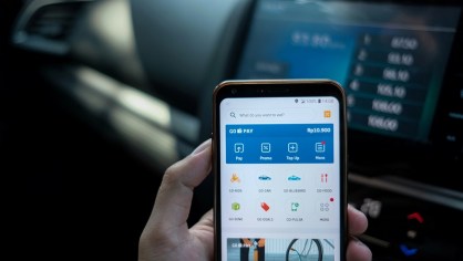 Pessoa segura celular com aplicativos de fintechs em frente a computador