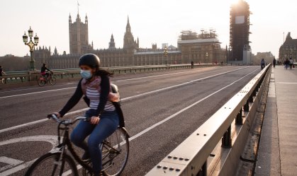 Mulher usa máscara enquanto pedala em frente ao Parlamento inglês, em Londres