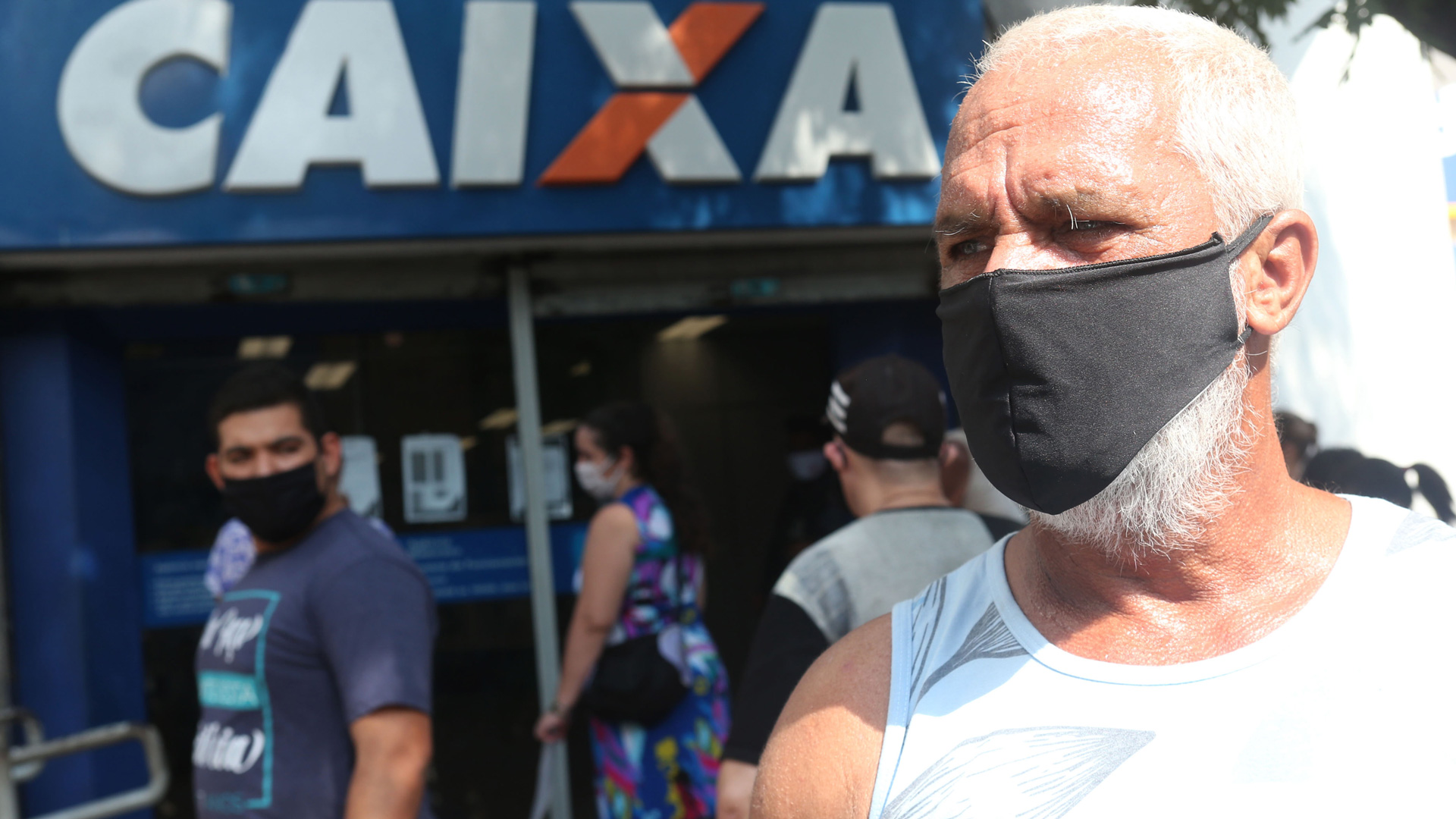 Homem de máscara em frente à aglomeração na agência da Caixa, no Rio. 