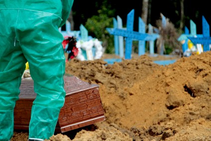 Coveiro em traje de proteção sepulta caixão em cemitério de Manaus