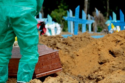 Coveiro em traje de proteção sepulta caixão em cemitério de Manaus