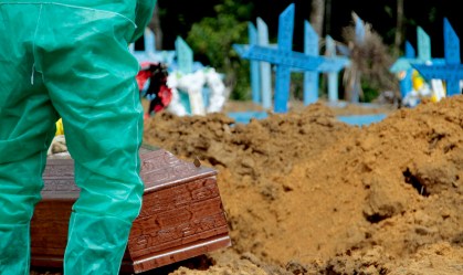Coveiro em traje de proteção sepulta caixão em cemitério de Manaus