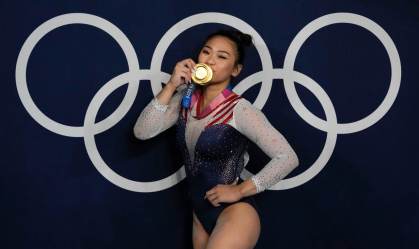 Sunisa Lee beija medalha em frente a painel com os arcos olímpicos, em Tóquio