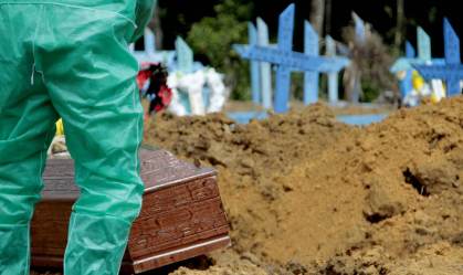 Coveiro em traje de proteção sepulta caixão em cemitério de Manaus