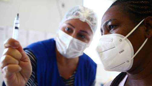 Enfermeira mostra vacina contra a Covid-19 para mulher no Rio de Janeiro