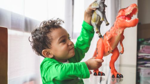 Criança brinca com bonecos de dinossauros