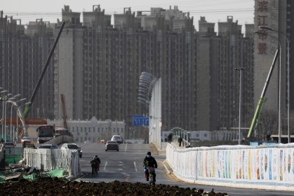 Homem anda de bicicleta próximo a um canteiro de obras perto de edifícios residenciais em Pequim, China.