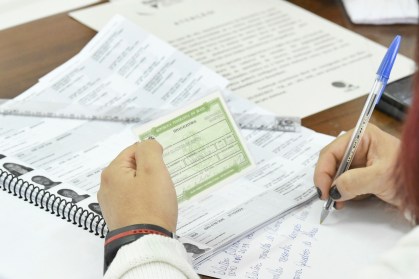 imagem de título de eleitor em primeiro plano sendo conferido por fiscal nas eleições