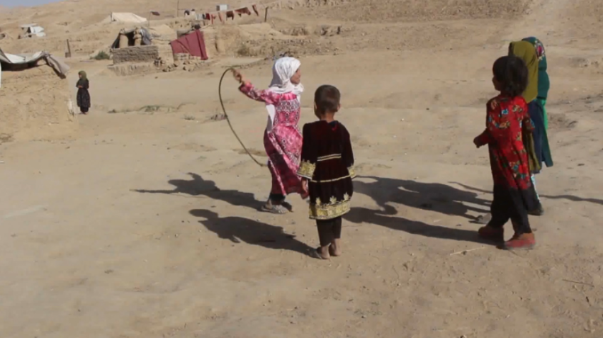 Parwana, 9, vestida de rosa, brinca com amigos no campo de desabrigados nos arredores de Qala-e-Naw, na província de Badghis, no Afeganistão/Reprodução/CNN