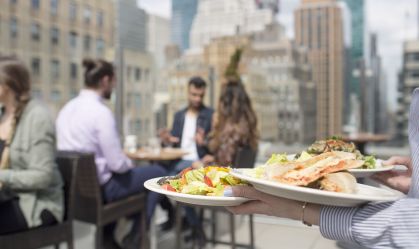 Waitress holding dishes while friends sitting against glass window at restaurant