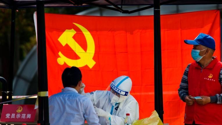 Um trabalhador médico testa um residente para Covid-19 em frente à bandeira do Partido Comunista da China na cidade de Zhenjiang, na província de Jiangsu / Foto: Chen Gang/VCG/Getty Images