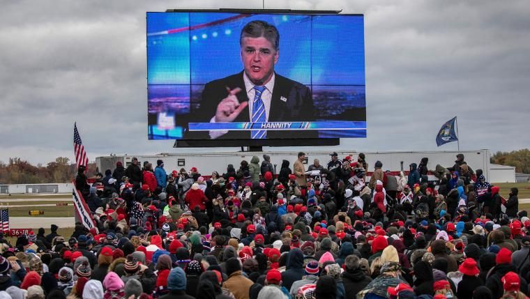 Apoiadores do presidente Donald Trump assistem a um vídeo com o apresentador da Fox News, Sean Hannity, antes da chegada de Trump a um comício de campanha em Michigan em 30 de outubro de 2020 / Foto: John Moore/Getty Images