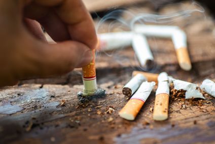 um mão aparece apagando uma bituca de cigarro em meio a outras