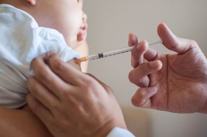 Uma mão injeta vacina em bebê