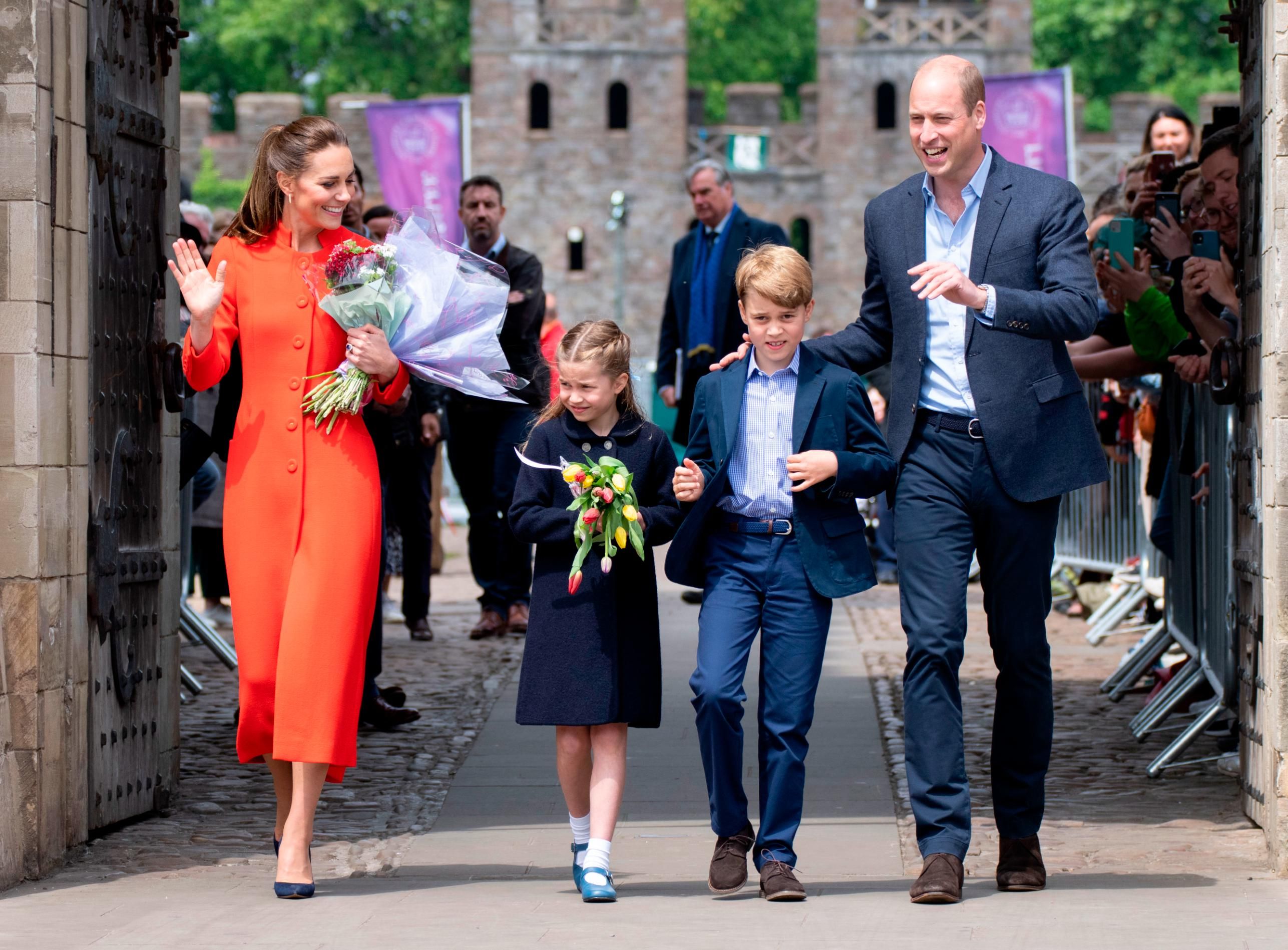 Em uma visita ao Castelo de Cardiff, o príncipe George combinou com seu pai, o príncipe William, um terno azul-marinho elegante, enquanto sua irmã, a princesa Charlotte, usava um casaco azul-marinho. Kate se destacou entre as paletas mais escuras em um casaco vermelho alaranjado / Mark Cuthbert/UK Press/Getty Images