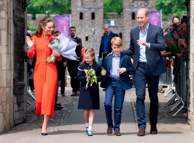 Em uma visita ao Castelo de Cardiff, o príncipe George combinou com seu pai, o príncipe William, um terno azul-marinho elegante, enquanto sua irmã, a princesa Charlotte, usava um casaco azul-marinho. Kate se destacou entre as paletas mais escuras em um casaco vermelho alaranjado / Mark Cuthbert/UK Press/Getty Images