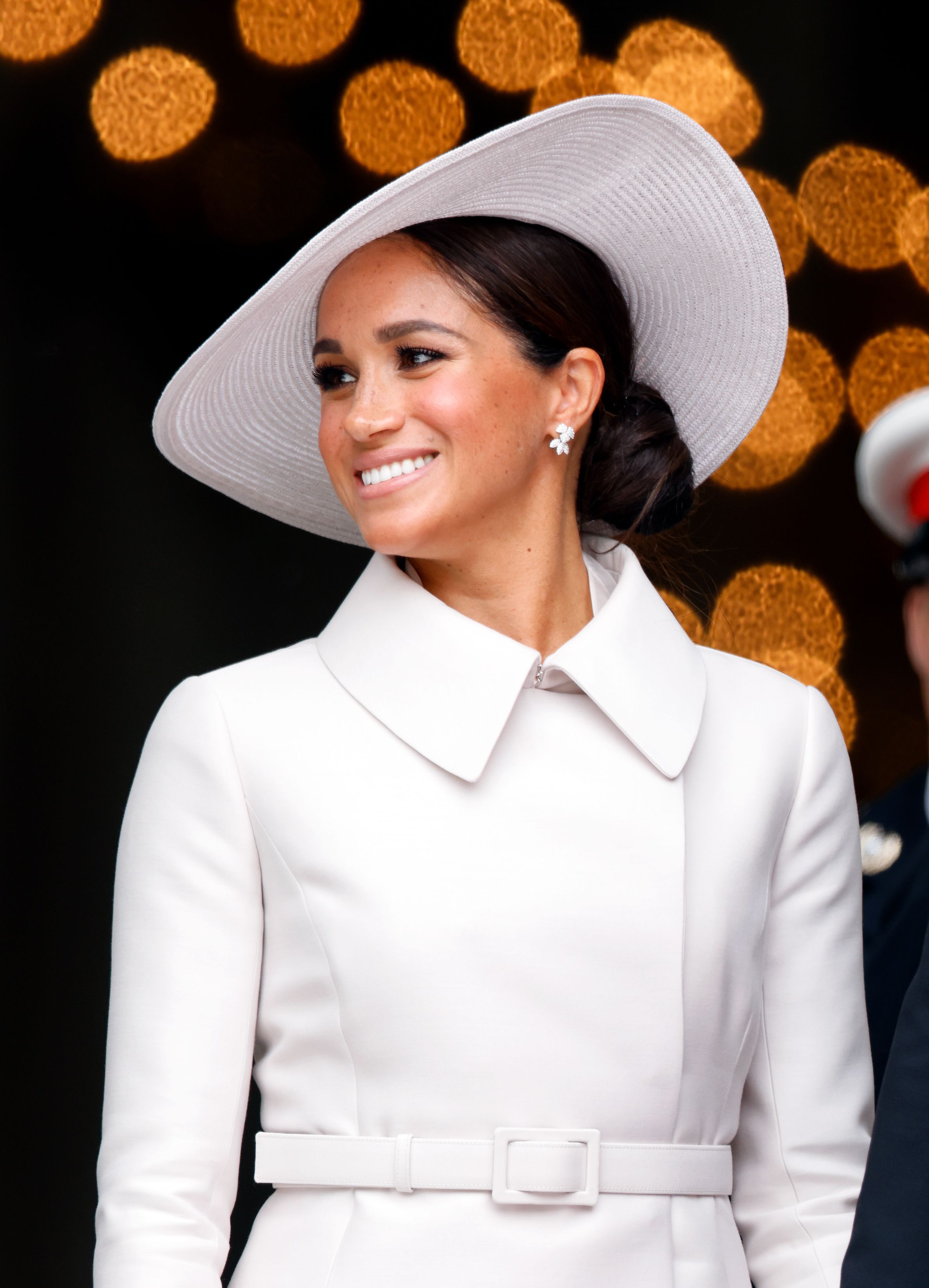 Vestida com um trench coat minimalista com cinto, Meghan, Duquesa de Sussex, escolheu um look Dior todo branco para sua aparição. Ela escolheu prender o cabelo para a ocasião por baixo de seu chapéu branco de abas largas de Stephen Jones / Getty Images