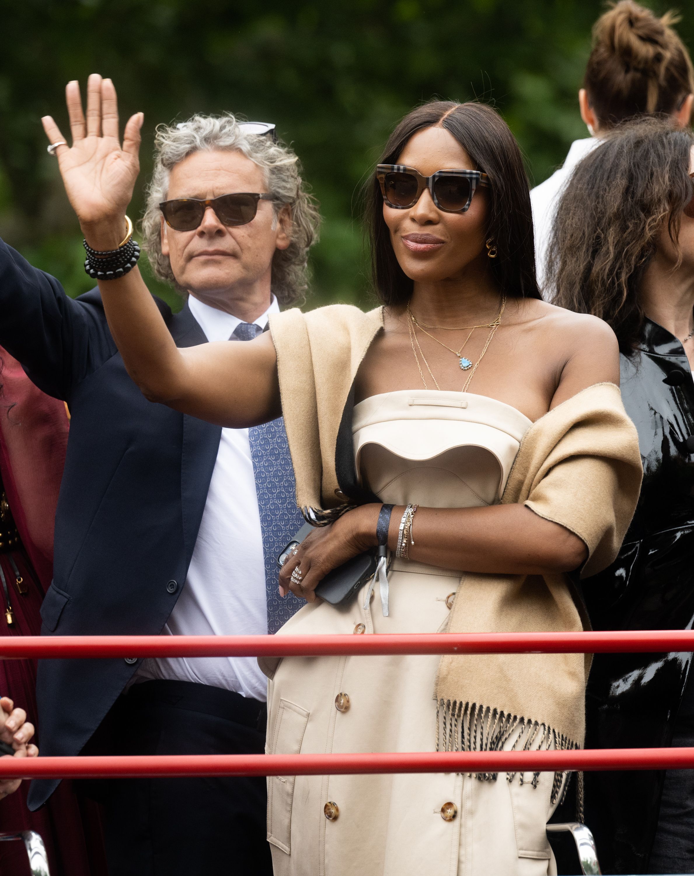 Naomi Campbell acenou para o público em cima de um dos carros alegóricos do desfile, usando um vestido Burberry, colares em camadas e um xale / WireImage