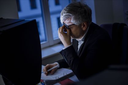 Homem com a mão no rosto enquanto está em frente ao computador no escuro