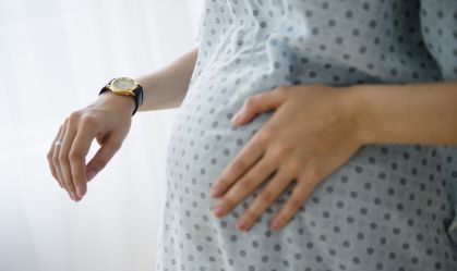 Mulher grávida com roupão de parto passando a mão na barriga