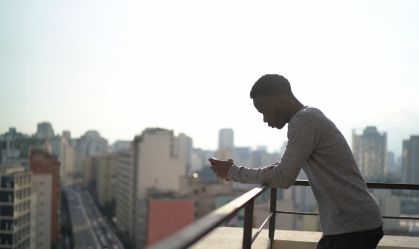 Jovem usando smartphone na varanda do apartamento