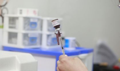 uma pessoa retirando o líquido do vidro de vacina com uma seriga