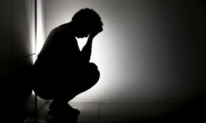 sombra de uma pessoa sentada com as mãos na cabeça abaixada encostada na parede