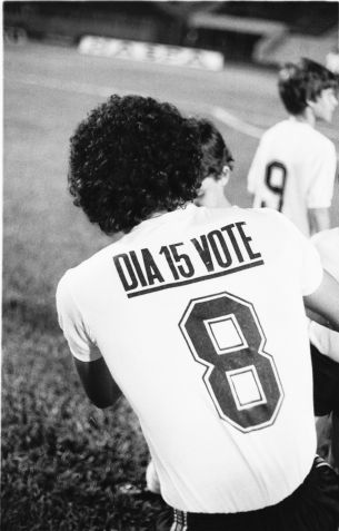 O jogador Sócrates dá autógrafo a torcedor e veste a camisa número 8 do Corinthians com a inscrição "Dia 15 Vote", na época da "Democracia Corinthiana", no jogo contra o Juventus, no estádio do Pacaembu, pelo Campeonato Paulista de Futebol, em novembro de 1982. • ANTONIO LÚCIO/ESTADÃO CONTEÚDO/AE