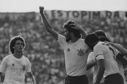 Sócrates comemora junto de outros jogadores do Corinthians um gol pelo Brasileirão de 1983, no estádio do Parque São Jorge (Fazendinha). A camisa dos jogadores estampava os dizeres &quot;Democracia Corinthiana&quot;