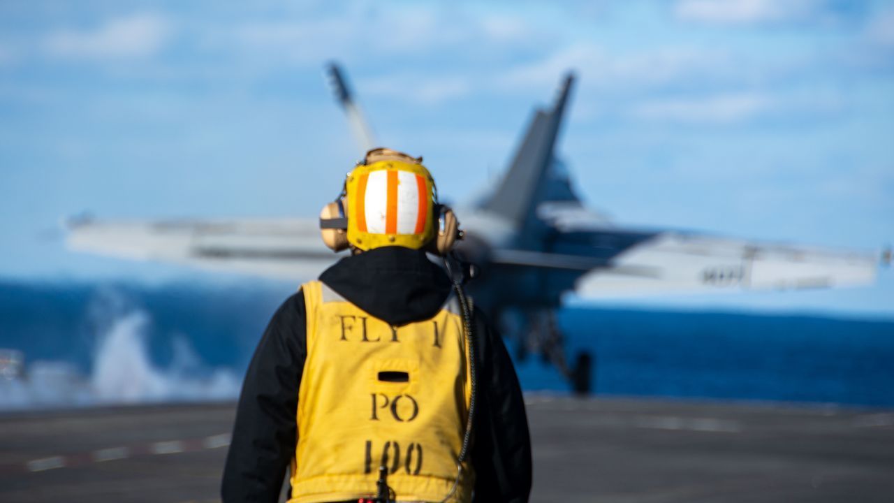 Trabalhador observa o lançamento de um F/A-18E Super Hornet a bordo de um porta-aviões dos EUA no Mar do Japão em 5 de outubro. / Marinheiro especialista em comunicação Natasha Chevalier Losada/Marinha dos EUA